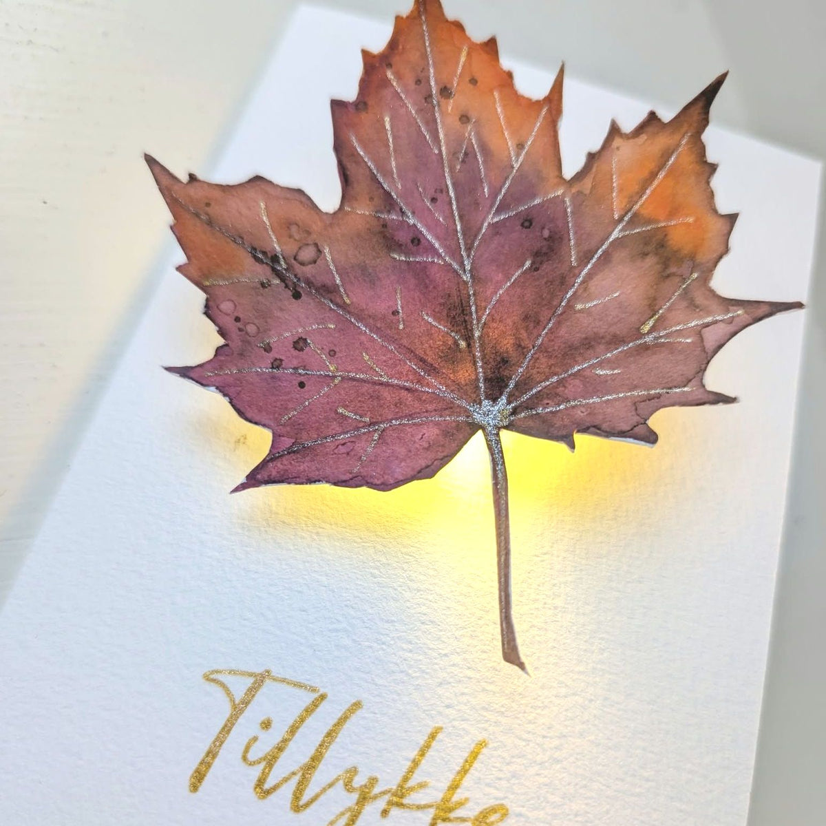 Detalje med starsparks gelpen af malet efterårsblad på kort med varmt LED-lys